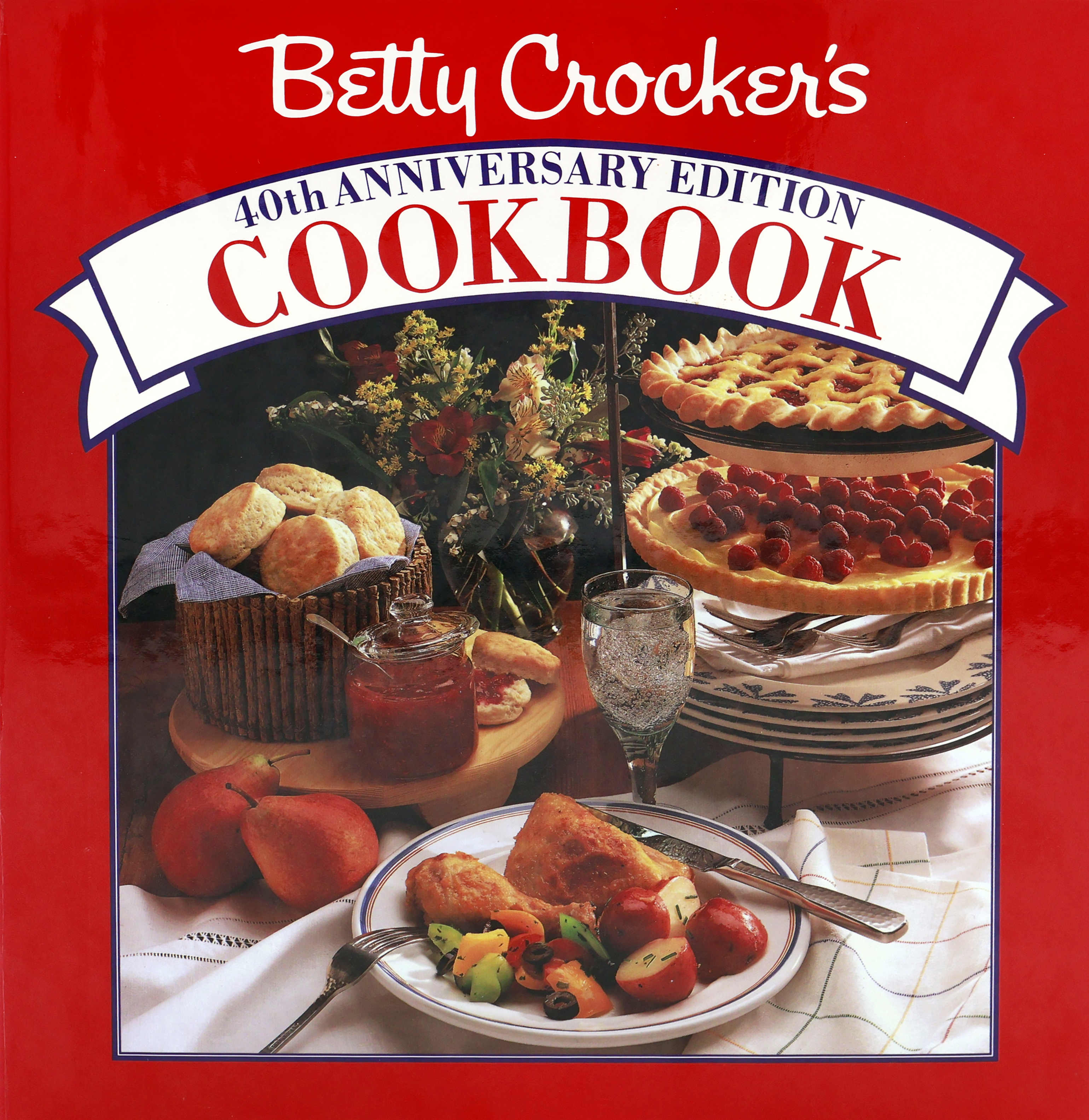 Cover of the 1991 Betty Crocker Cookbook with a red cover that has a “40th Anniversary” banner with square below with plate of roast chicken and small red potatoes, biscuits and jam, vase of flowers, and a tiered plate holder with plates on the lowest tier; a tart on the 2nd tier; cherry pie on the top tier.